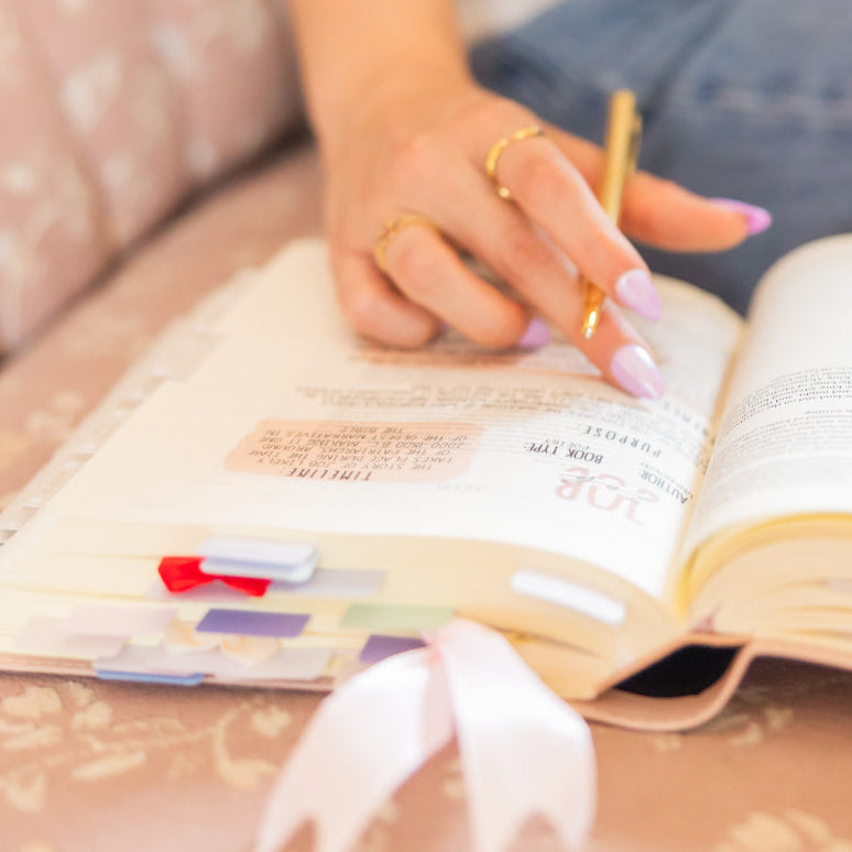 Person reading the bible with a pen and highlighter, sitting on a couch.