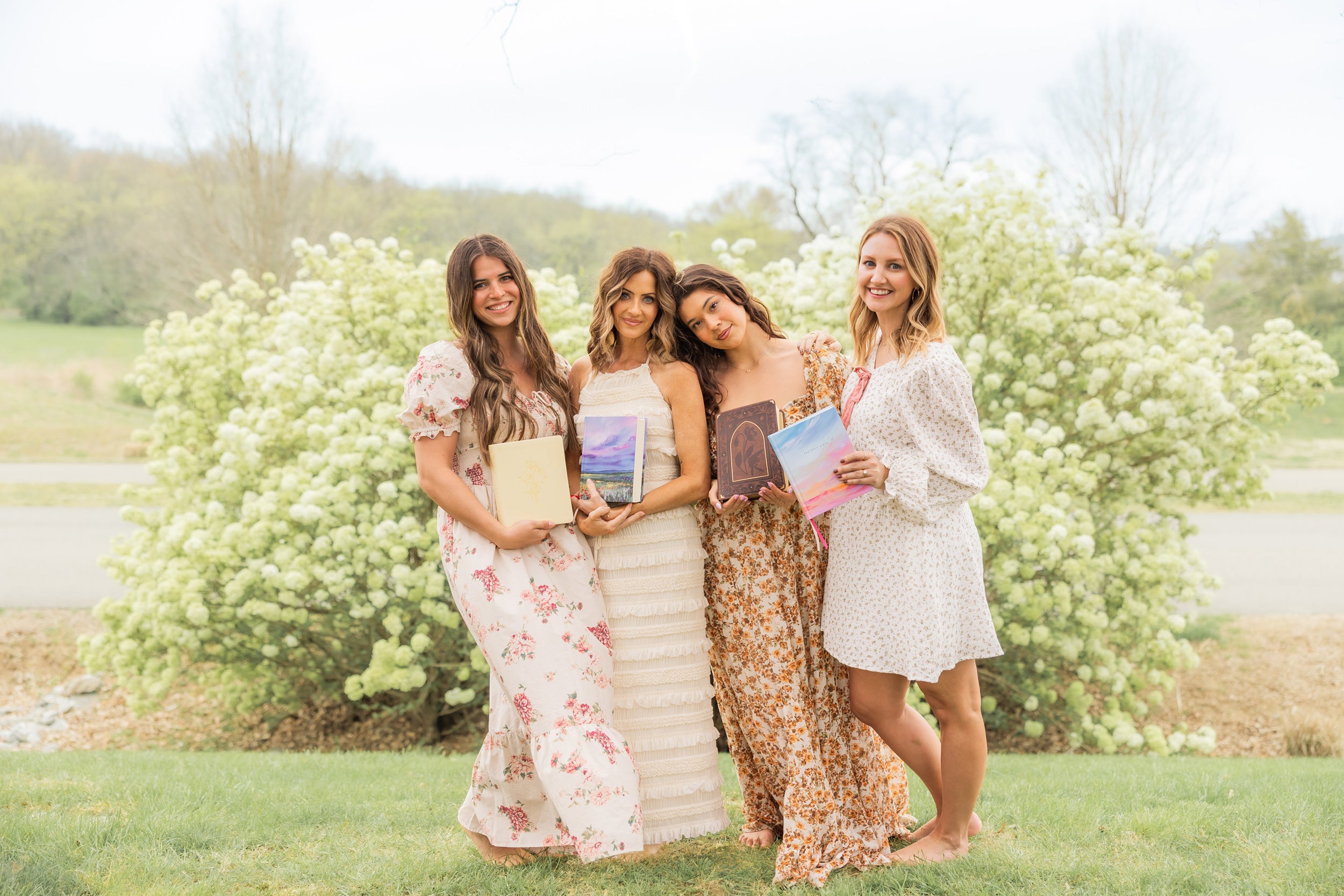 Four women standing outdoors in front of a flowering bush, holding bibles.